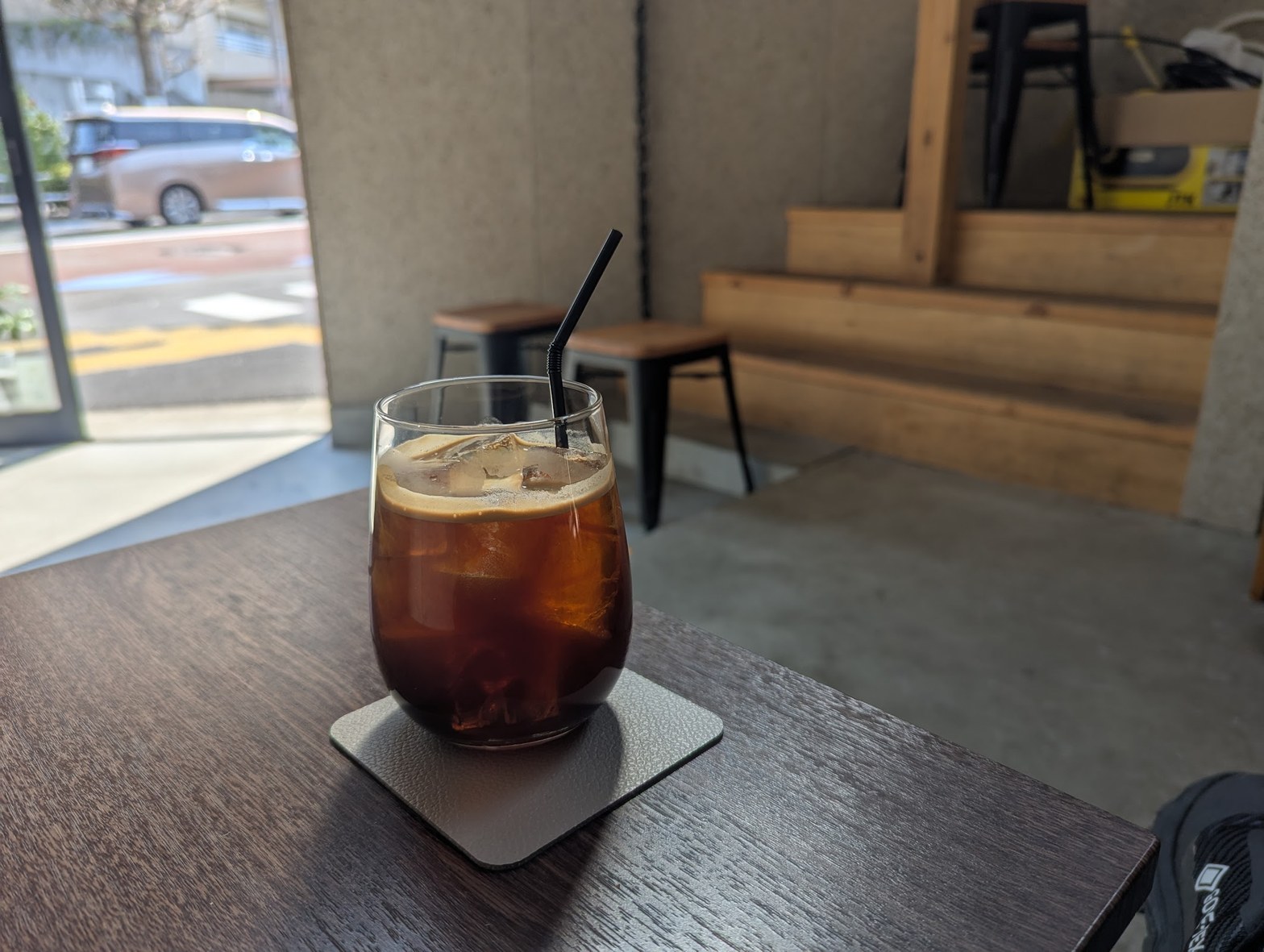 グラスに氷とアイスコーヒーが注がれ、コースターの上に置かれた窓際のテーブル席。