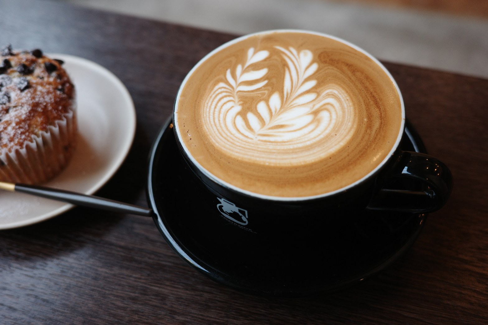 黒いカップに注がれたラテアートのカフェラテと、チョコチップマフィンが白皿に乗り並ぶ。
